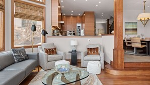 A modern living room with a sofa, armchairs, a glass coffee table, and a dining area with a table and chairs.