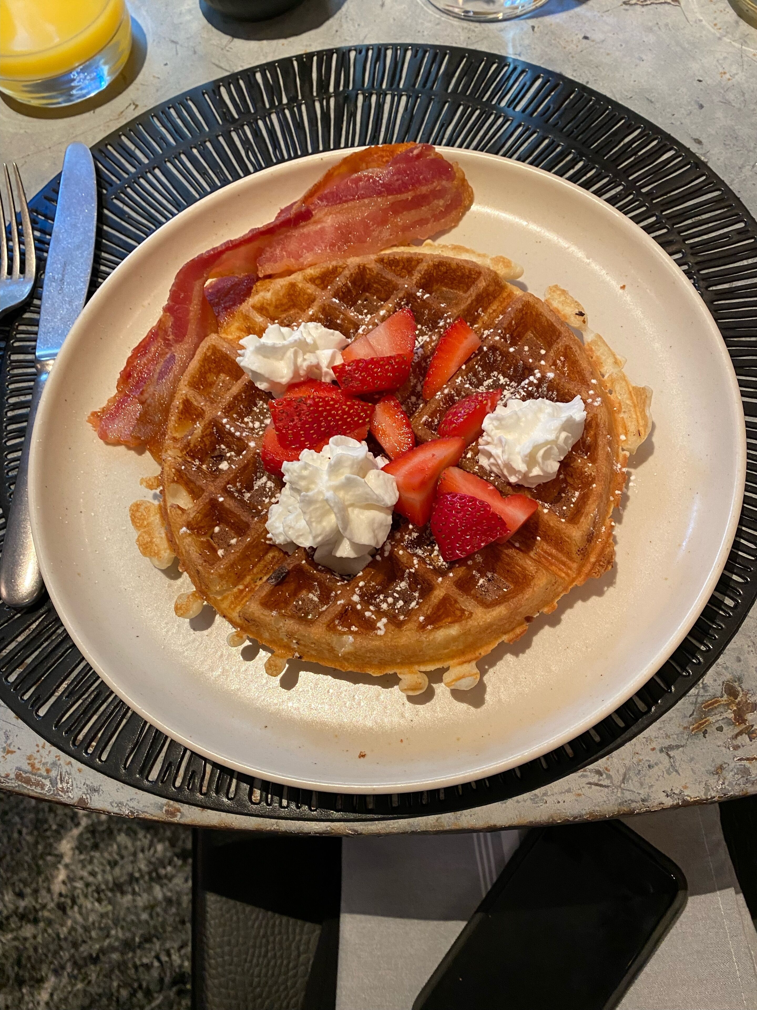 Um prato de waffles coberto com morangos, chantilly e bacon.
