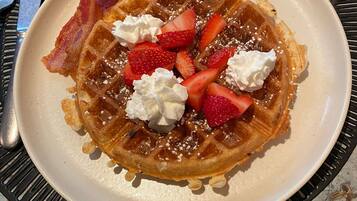 Um prato de waffles coberto com morangos, chantilly e bacon.