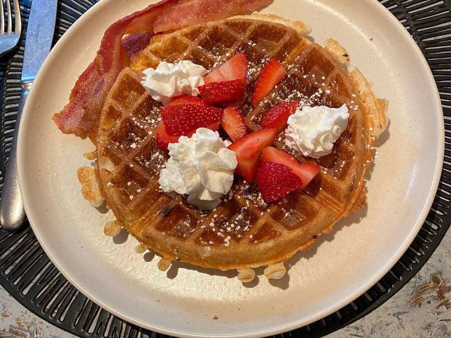 Um prato de waffles coberto com morangos, chantilly e bacon.