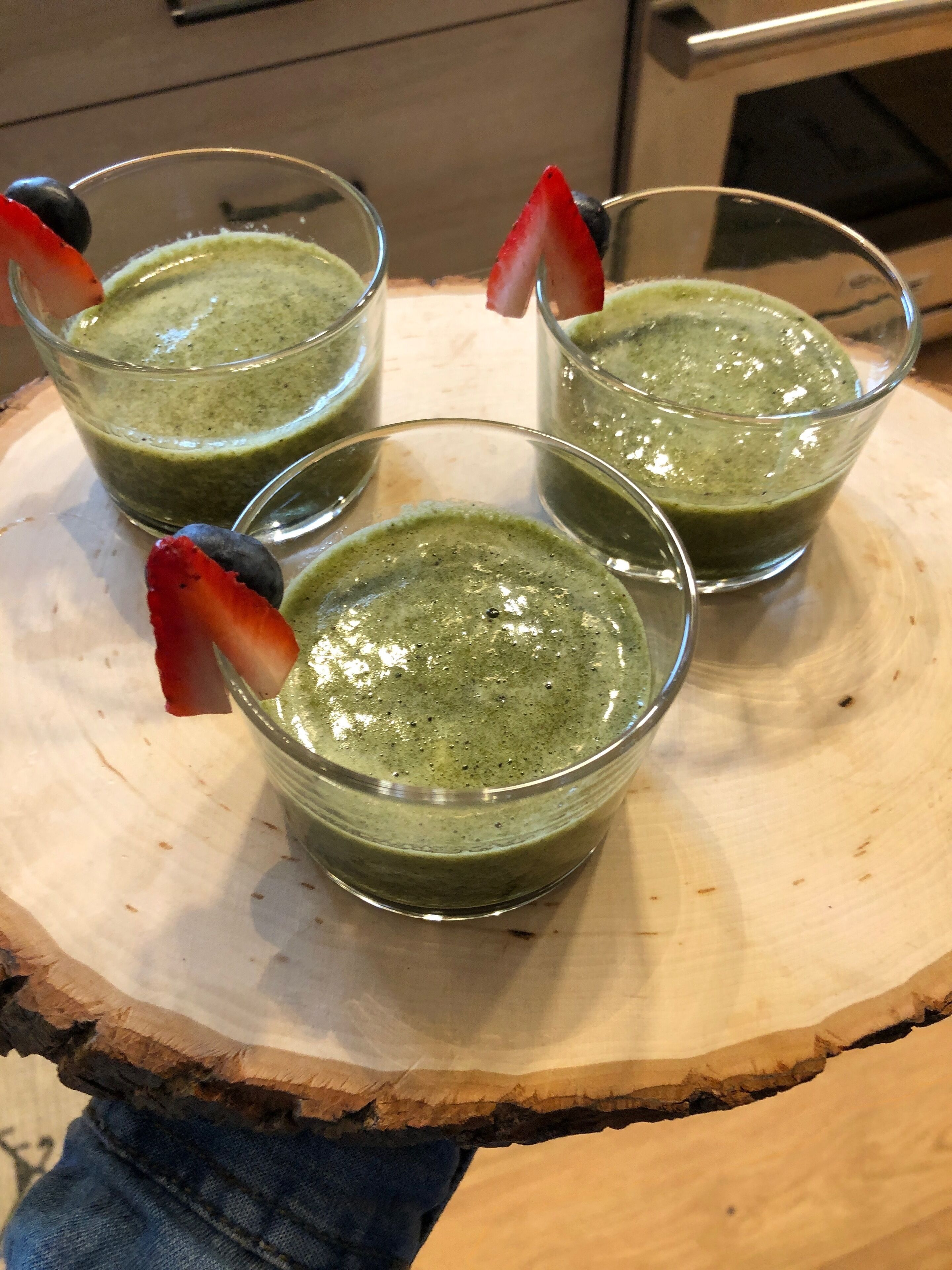 Three glasses of green smoothie on a wooden board.