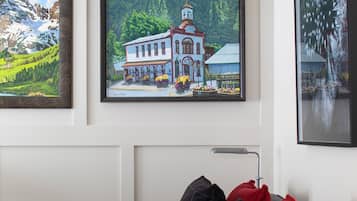Una sala de estar con un sofá gris, cojines rojos y de cuadros, una mesita y un cuadro enmarcado de una casa con una torre del reloj.