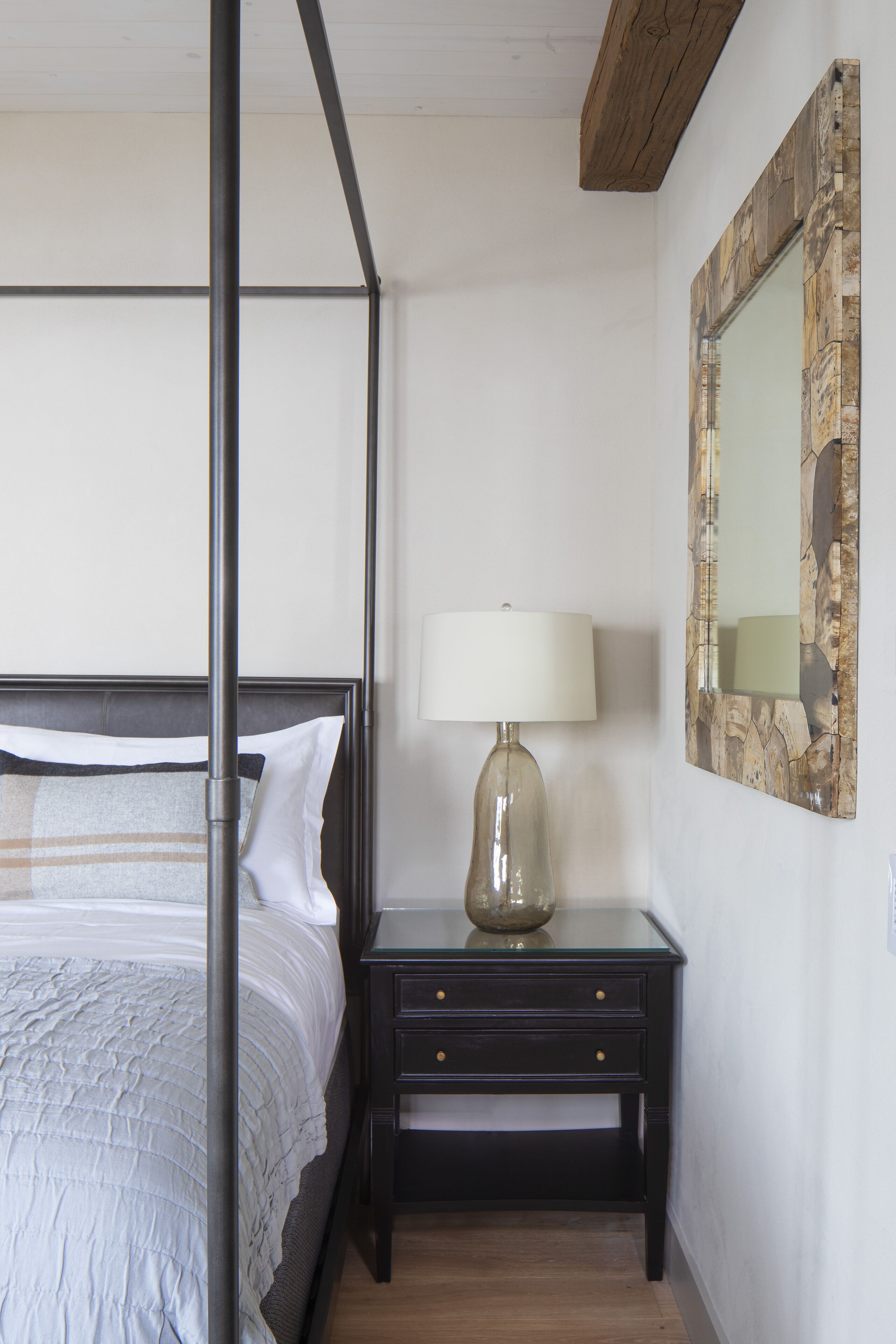 Un dormitorio con una cama con dosel, una mesita de noche con lámpara y un espejo en la pared.