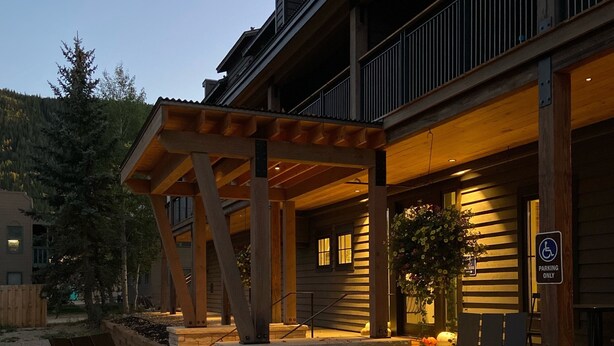 A covered outdoor seating area with a fire pit, wooden chairs, and a building with a balcony. - Vaquera House (Crested Butte)