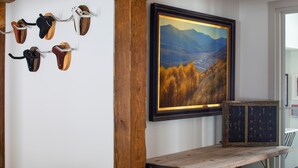 A room with a wooden bench, a wall-mounted shoe rack, a framed landscape painting, and a chalkboard with words. - Vaquera House (Crested Butte)
