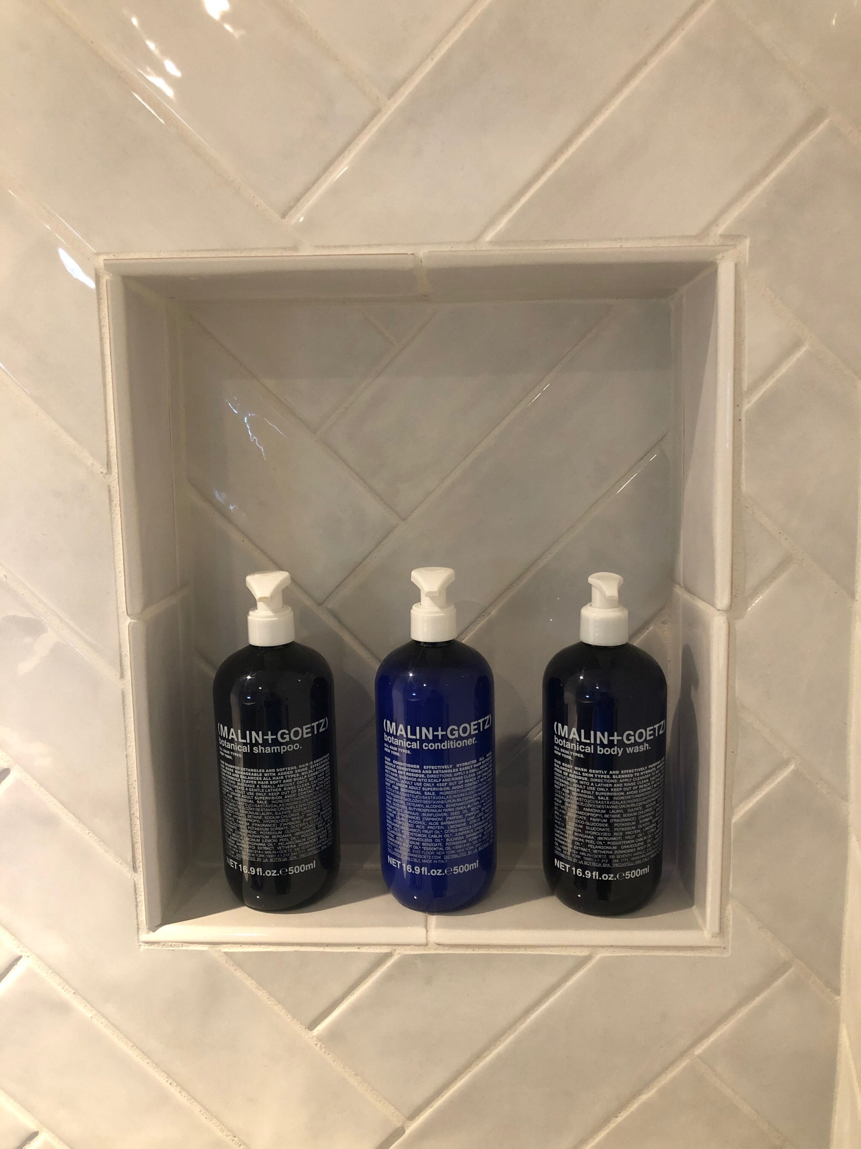 A bathroom shelf with three bottles of MALIN+GOETZ products.