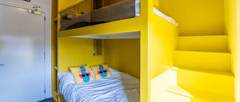 A room with a bunk bed, a single bed, and a staircase.