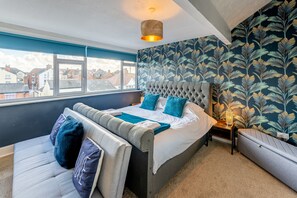 A bedroom with a large bed, a bench, a nightstand, and a window with a view of buildings. - Blackpool Abode The Cinema House (Blackpool)