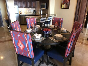 Une table à manger dressée pour six personnes, avec des chaises assorties, une cuisine en arrière-plan et un tableau accroché au mur.