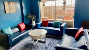 Ein Zimmer mit blauen Wänden, einem blauen Sofagarnitur, einem weißen Couchtisch und einem großen Fenster mit weißen Vorhängen.