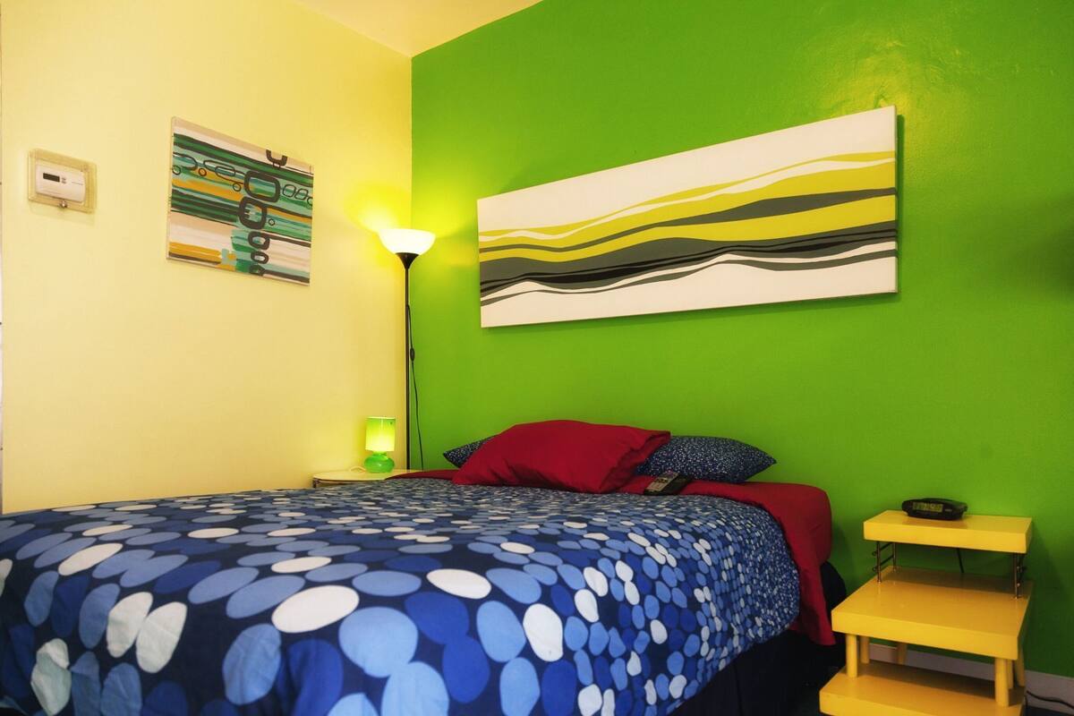 Une pièce comprenant un lit, une table de chevet, une lampe, un tableau et une horloge murale.