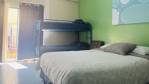 Ein Zimmer mit einem Etagenbett, einem Einzelbett, einer grünen Wand und einem Fenster mit Vorhängen.