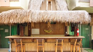 Eine Tiki-Bar mit Strohdach, Holzbalken und vier Barhocker.