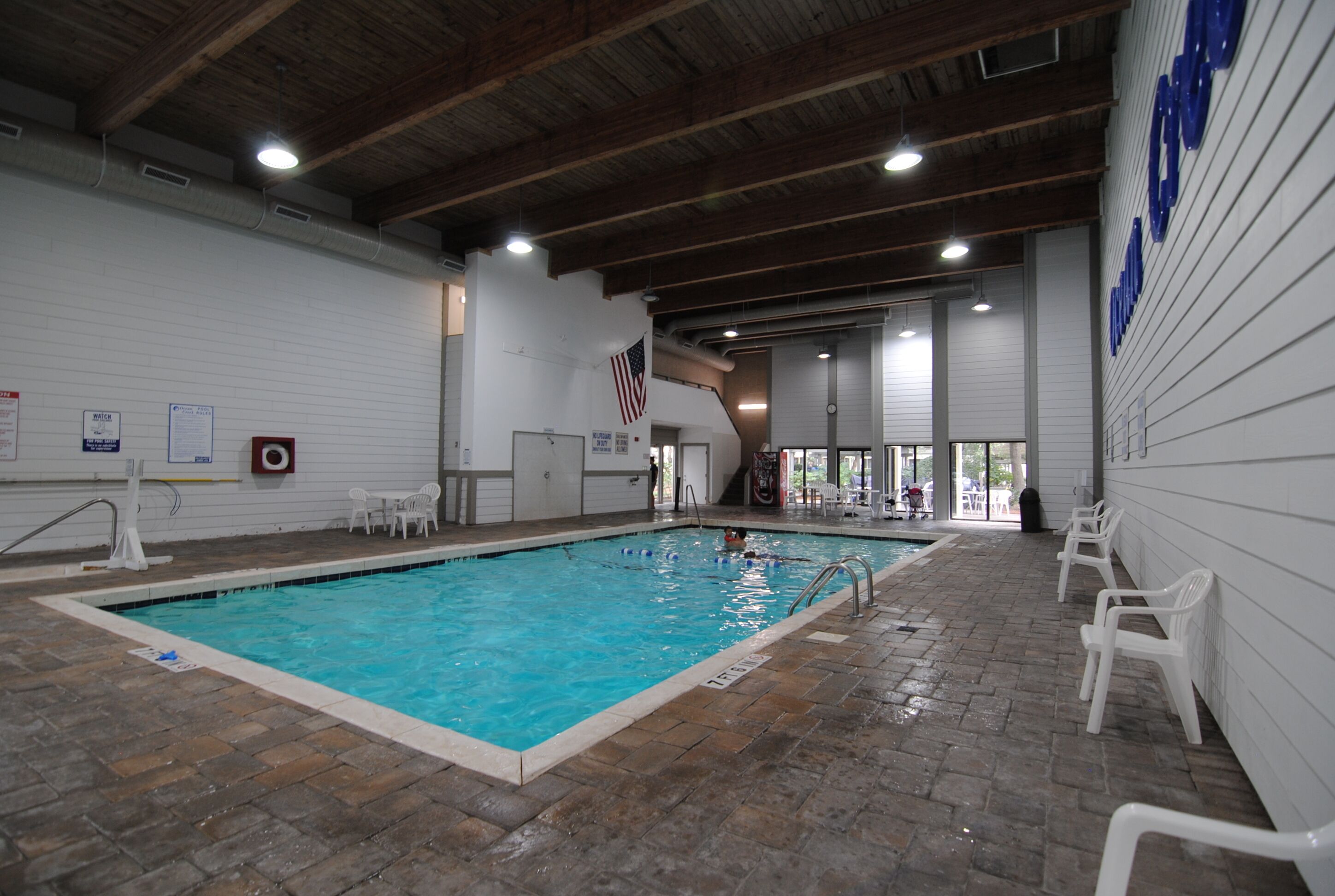Une piscine intérieure avec un sol carrelé, des murs blancs et un plafond en bois.