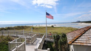 A wooden deck with a white railing overlooking a beach with an American flag. - OASIS BEACH RETREAT NORTH MYRTLE BEACH (Myrtle Beach)
