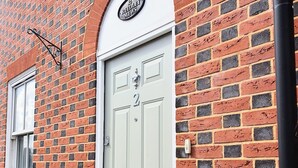 A light grey door with the number 2, a brick wall, and a small window to the left. - Charming Mews House in the Heart of Lymington (Lymington)