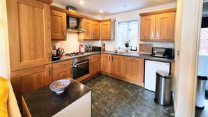 A modern kitchen with wooden cabinets, a gas stove, a microwave, and a dishwasher. - Charming Mews House in the Heart of Lymington (Lymington)