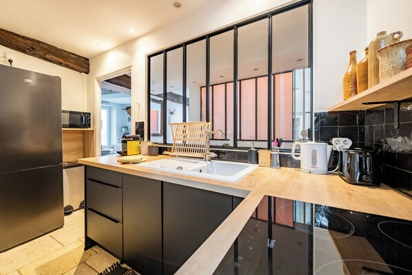 A modern kitchen with a black refrigerator, wooden cabinets, a sink, and a coffee maker.