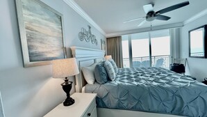 Une chambre à coucher comprenant un lit, une commode, un ventilateur de plafond, une grande fenêtre et un balcon.
