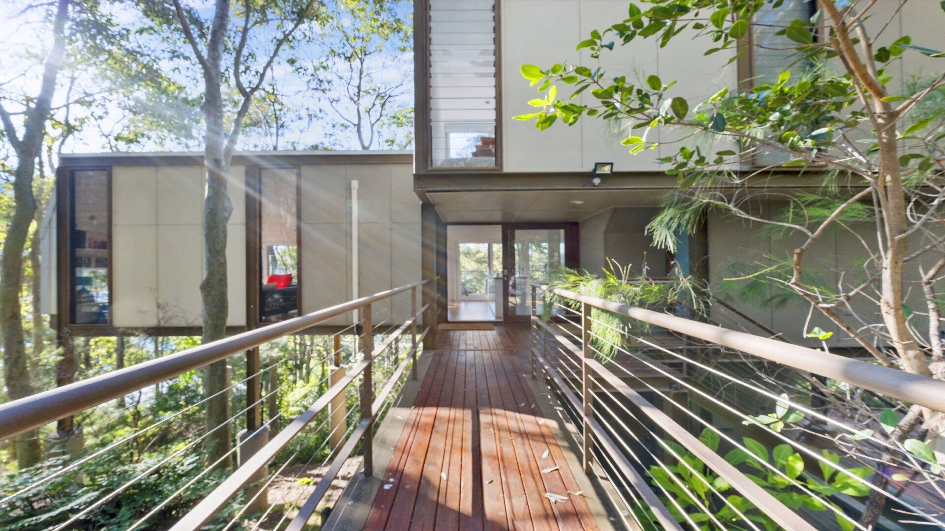 A wooden bridge leading to a modern building with glass doors and a view of trees.