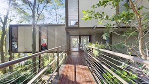 A wooden bridge leading to a modern building with glass doors and a view of trees.