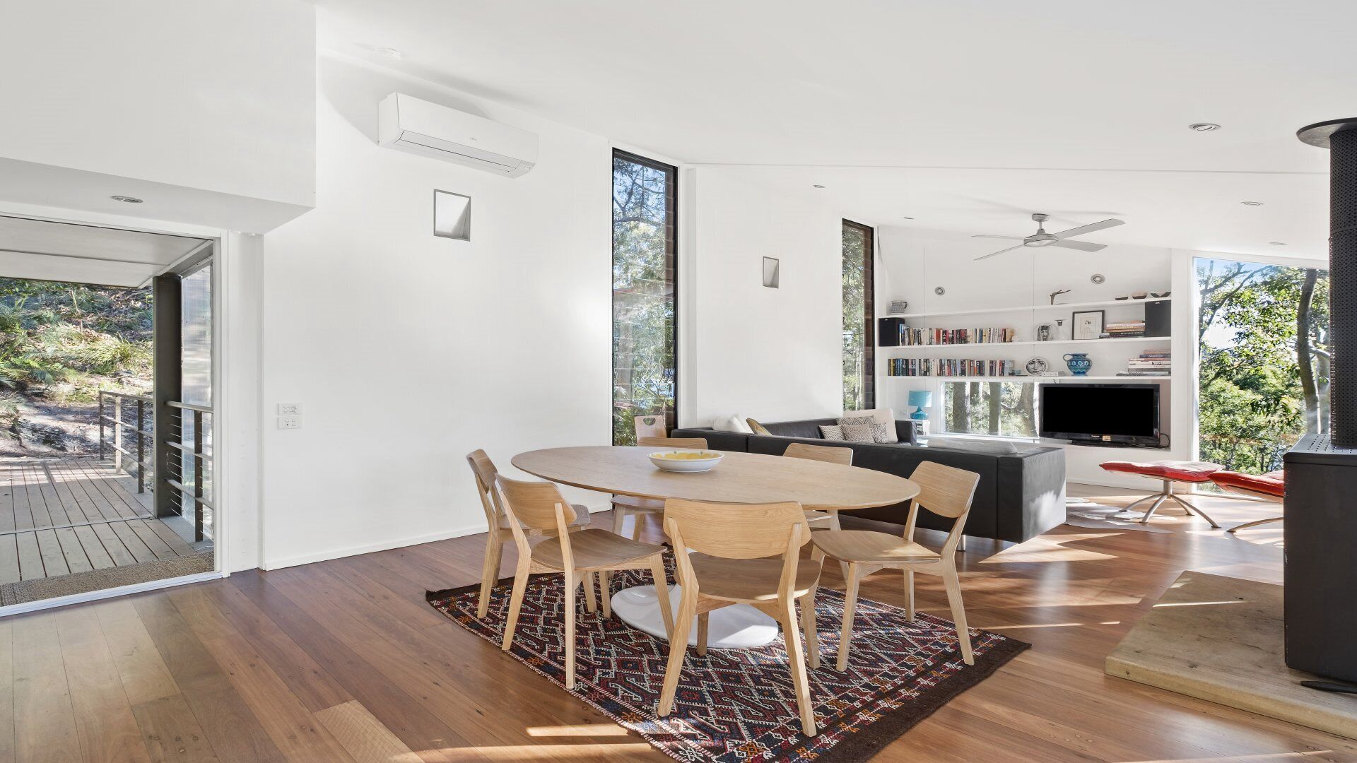 A modern living room with a wooden dining table, chairs, a sofa, and a TV.