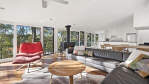 En moderne stue med pejs, en rød lænestol, en sofa og et spiseområde med et køkken i baggrunden.