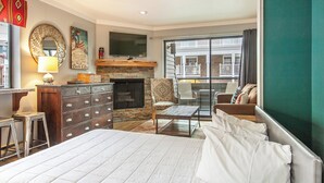 A bedroom with a large bed, a fireplace, a TV, and a balcony with a view of a building. - Lodge at Mtn Village A222 | Ski-In/Out | Hot Tub | Plaza View | PCMR | Pool (Park City)