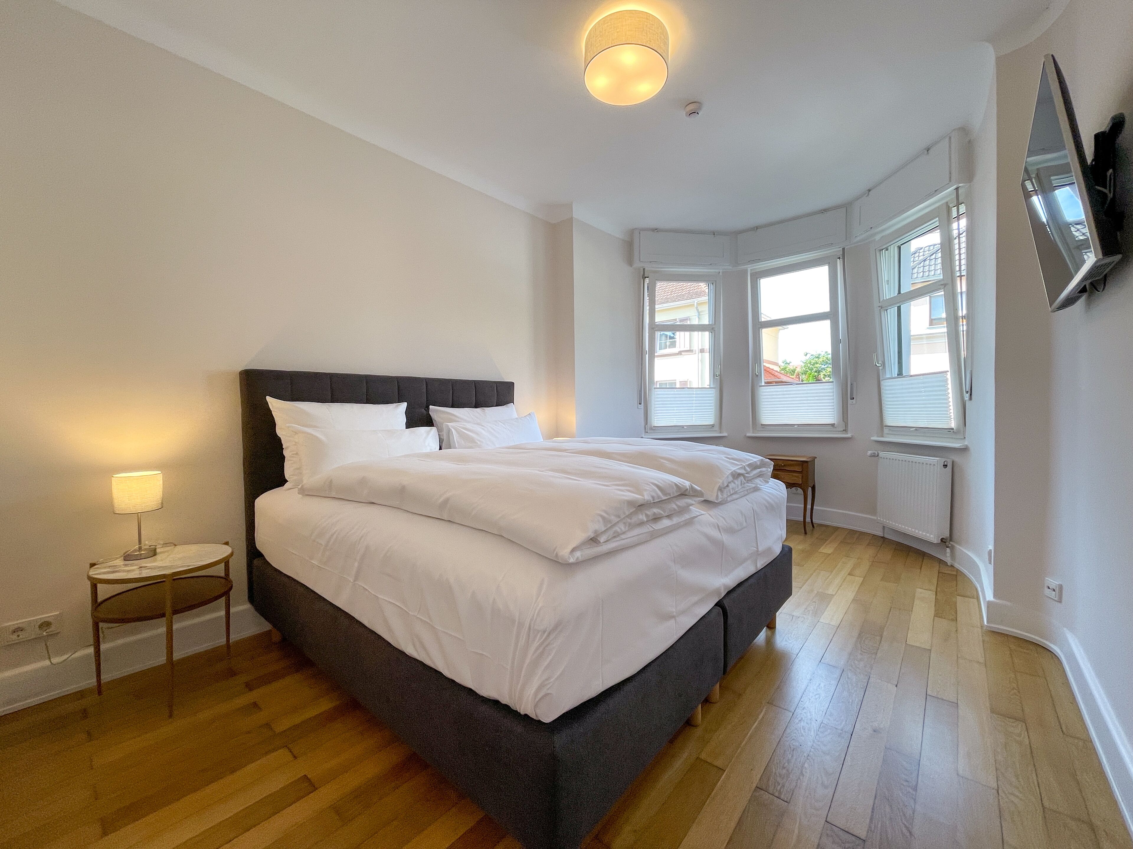 A bedroom with a large bed, a bedside table with a lamp, and a TV mounted on the wall.