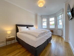 A bedroom with a large bed, a bedside table with a lamp, and a TV mounted on the wall.