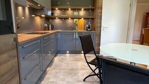 A modern kitchen with a central island, built-in appliances, and a dining area with a glass table and chairs. - Saar-Apartments (Merzig)