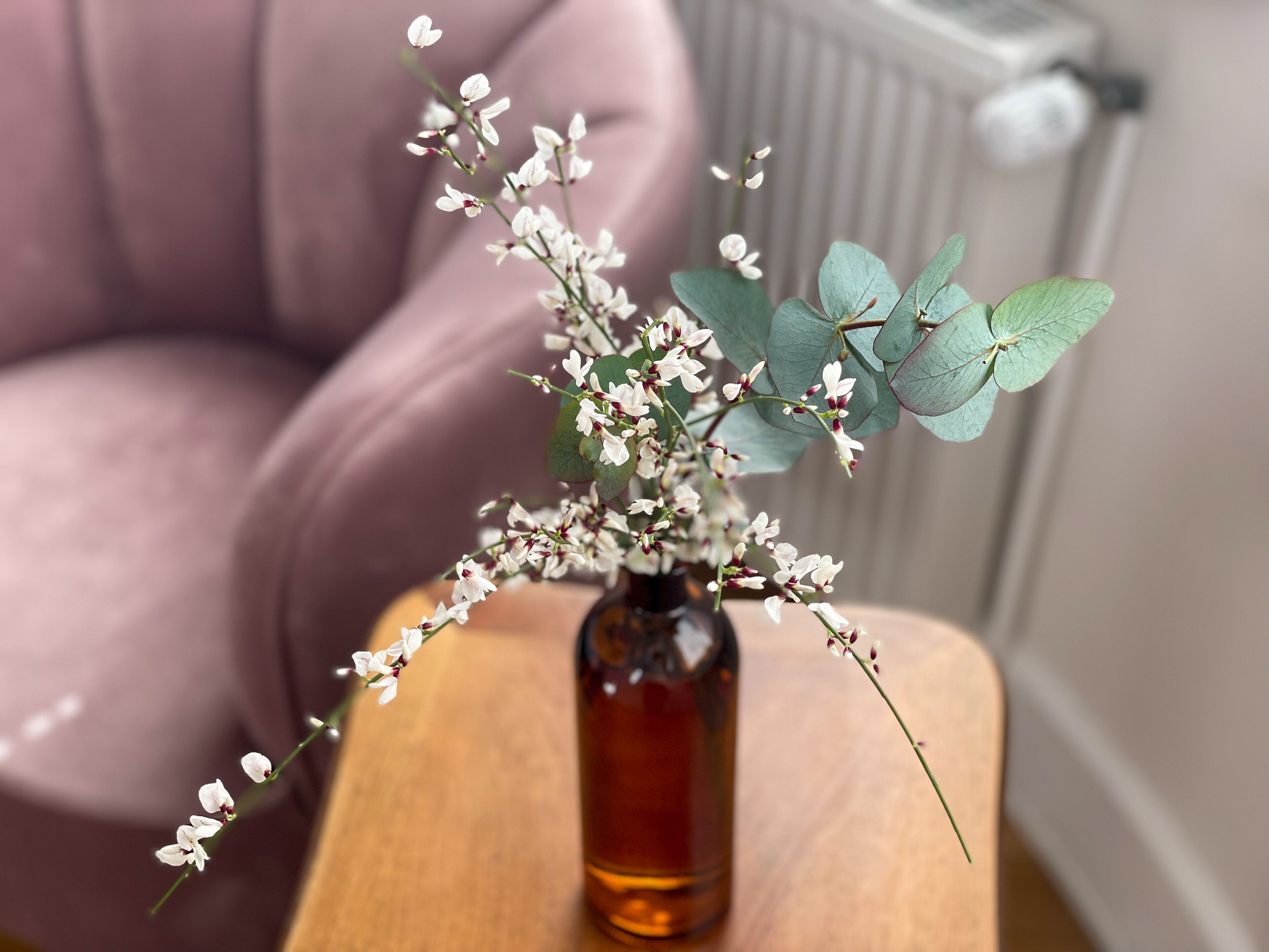 Un vase contenant des fleurs blanches et des feuilles vertes, posé sur une table en bois.