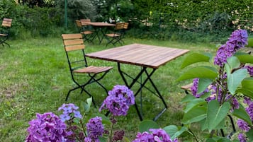 A garden with a wooden table and chairs, surrounded by greenery and purple flowers.