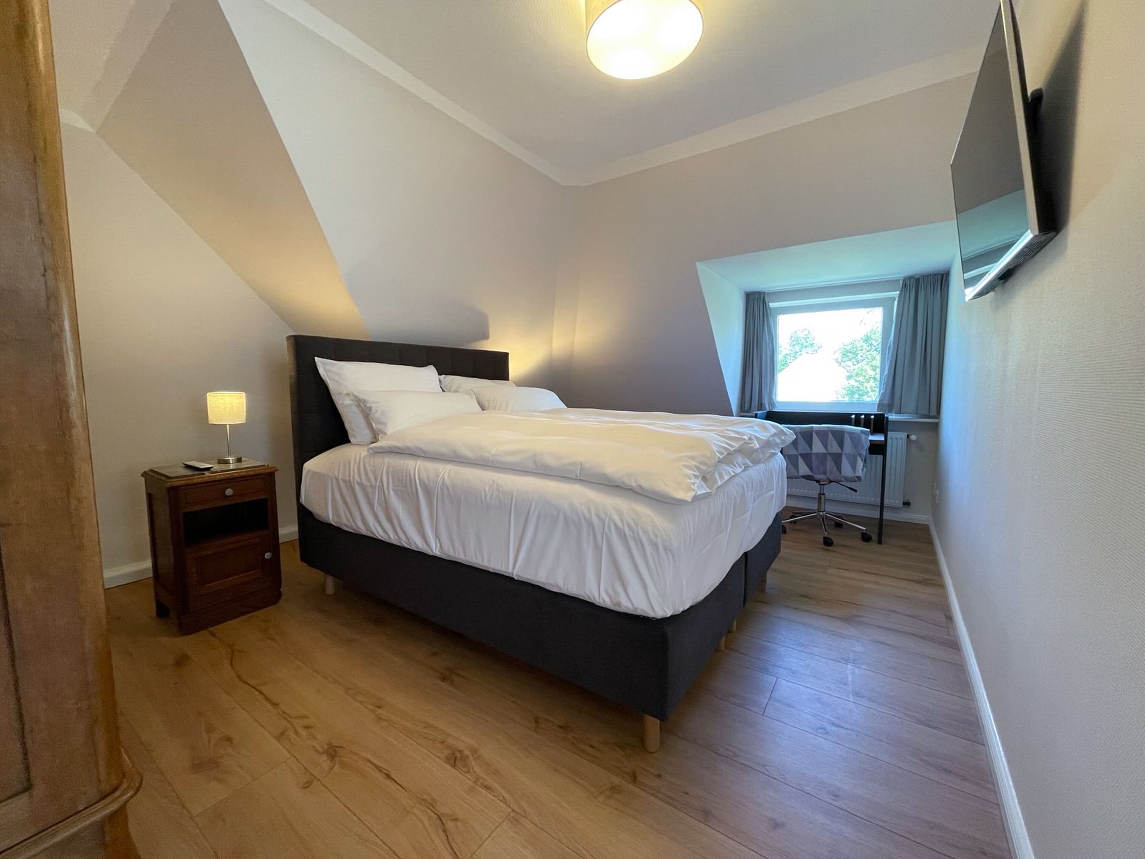 Une chambre à coucher comprenant un lit, une table de chevet, un bureau et un téléviseur fixé au mur.