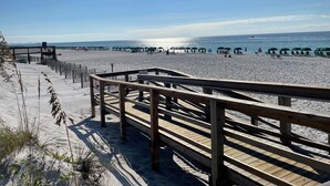 Een houten looppad dat naar een zandstrand leidt, met parasols en strandstoelen.
