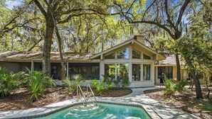 Une maison avec une piscine, entourée d’arbres et de plantes.