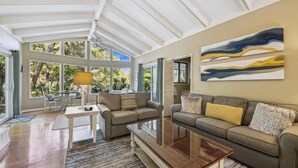 Un salon spacieux doté d’une grande porte vitrée donnant sur un jardin, d’une table basse en bois et d’un canapé gris agrémenté de coussins.