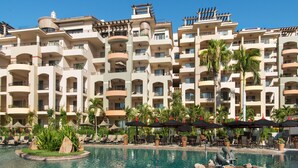 Un hôtel doté de nombreux balcons, d’une piscine avec des chaises longues et de palmiers.