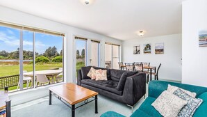 Un salon spacieux avec une grande fenêtre, un canapé gris foncé, un fauteuil turquoise et une table basse en bois.