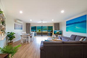 Ett rymligt vardagsrum med ett stort fönster, en soffa, ett matbord och en TV.