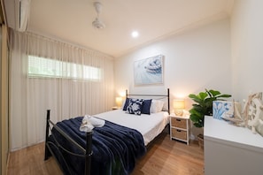 A bedroom with a bed, bedside tables, a wall-mounted artwork, and a potted plant.