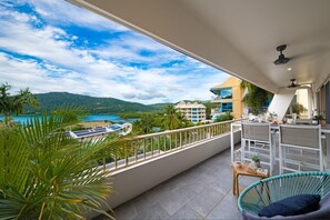 A balcony with a view of a beach and mountains, a chair, a table, and a bar area. - Eagles Nest On Airlie (Airlie Beach)
