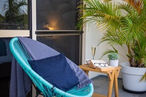 Ein Zimmer mit einem türkisfarbenen Sessel, einem kleinen Holztisch mit einem Buch und Gläsern sowie einer Topfpflanze.