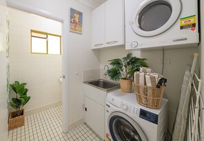Une petite buanderie comprenant un lave-linge, un évier et une plante en pot.