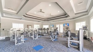Ein Fitnessstudio mit unterschiedlichen Trainingsgeräten, darunter Laufbänder und Kraftgeräte, Teppichböden und Deckenventilatoren.