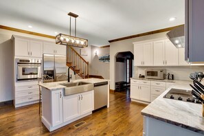 A modern kitchen with white cabinets, stainless steel appliances, a marble countertop, and a wooden staircase.