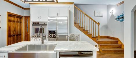 A kitchen with a central island, stainless steel appliances, and a wooden staircase leading to another level.