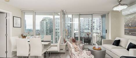 A modern living room with a dining area, large windows, and a city view.