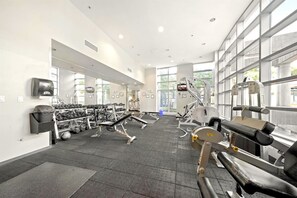 Un gimnasio con diverso equipo de ejercicio, ventanas amplias y un espejo en la pared.