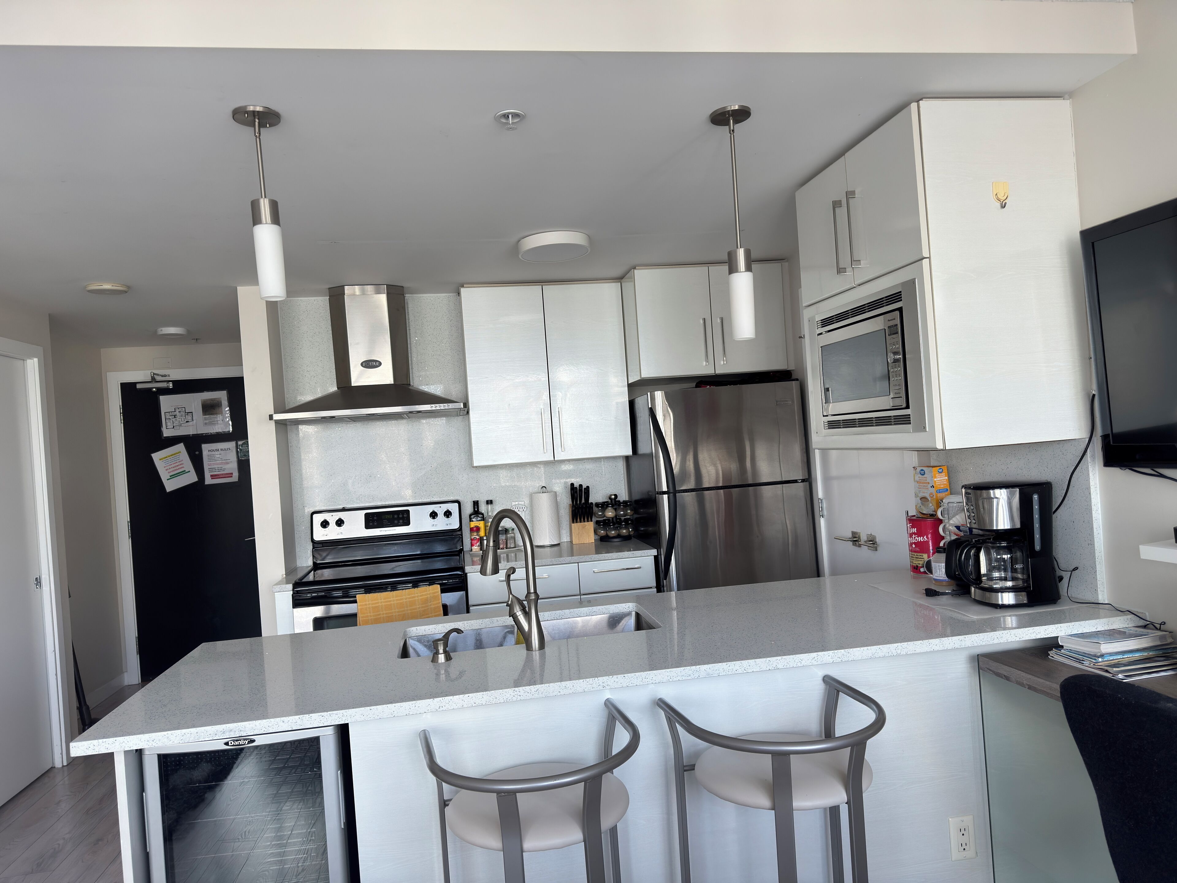 Una cocina moderna con electrodomésticos de acero inoxidable, una isla central con taburetes de bar y armarios blancos.